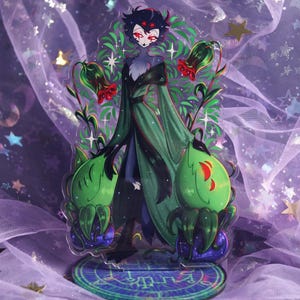 May include: An acrylic figure featuring a character with red eyes, black hair, and a green and black outfit. The figure is surrounded by green plant-like elements with red accents and rests on a patterned base. The background is a purple fabric with stars.