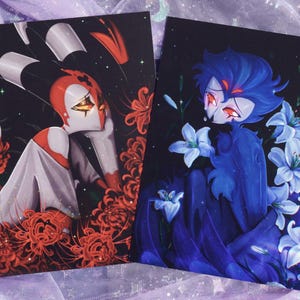 以下が含まれることがあります： 暗い背景に、様式化されたキャラクターが描かれた2つのアートプリント。1つのプリントは、赤い花を持つ赤、白、黒のキャラクターを示しています。もう1つは、白いユリを持つ青いキャラクターを描いています。