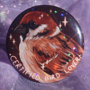 Puede incluir: Un botón redondo con una ilustración detallada de un gorrión. El ave tiene plumas marrones, blancas y negras. El botón tiene el texto "CERTIFIED BIRD LOVER" en blanco, con acentos de estrellas.