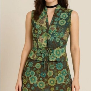 May include: A sleeveless floral print top and matching skirt. The outfit features a brown base with teal and green floral patterns. The top has a V-neck and tie closure. The skirt has a sheer brown hem.