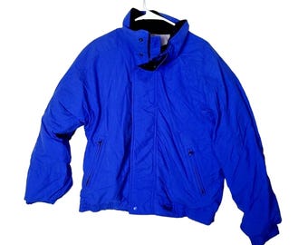 May include: A bright blue jacket with a black collar and zip pockets. The jacket is suspended from a white hanger. The jacket has a button closure and a black lining.