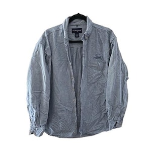 May include: A light blue button-down shirt with long sleeves, hanging on a black hanger. The shirt has a subtle striped pattern and a small embroidered logo on the chest. The collar is buttoned down.