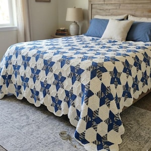 May include: A handmade crochet bedspread featuring a repeating star pattern in cream, solid blue, and a variegated blue and grey yarn. The blanket has a scalloped edge and is displayed on a bed, with a silver measuring tape placed on the floor.