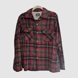 May include: A red, black, and gray plaid flannel shirt with two chest pockets and a collared neckline. The long-sleeved shirt is button-down and hangs on a beige hanger.