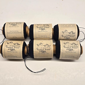 May include: Six spools of navy blue thread labeled "Raphael Brand Gimp" with text indicating they are for crocheting, knitting, and embroidery. Each spool has a paper label with an illustration of cherubs. The thread is wound around a wooden core.