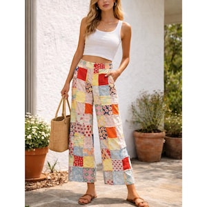 May include: A woman wearing a white tank top and patchwork pants. The pants are a mix of colorful fabric squares in various patterns. She is holding a woven tote bag and wearing brown sandals.