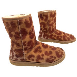 Puede incluir: Un par de botas marrones y beige con estampado de leopardo. Las botas tienen la punta redondeada y una suela beige. El interior de las botas está forrado con un material color crema.