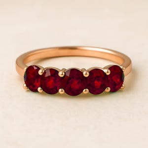May include: A rose gold ring with five vivid red gemstones. The gemstones are round and set in individual prongs. The band is smooth and polished. The ring's design offers a classic and elegant look, suitable for various occasions.
