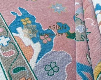May include: Close-up of a pink handmade rug with a floral pattern. The rug features blue, orange, green, and purple floral designs. The text "ASIAN HANDMADE RUGS" is visible on the rug.