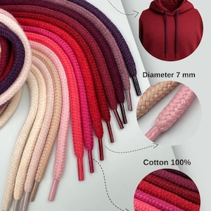 Puede incluir: Una colección de cordones de capucha coloridos en tonos rojos, rosas y morados. La imagen muestra los cordones con un diámetro de 7 mm, hechos de 100% algodón. También se ve el texto "Great for hoodies".