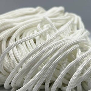 Puede incluir: Primer plano de un montón de cordón trenzado blanco. Los cordones están tejidos apretadamente y parecen estar hechos de un material sintético. Los cordones están apilados, con algunos cordones enfocados y otros borrosos en el fondo.