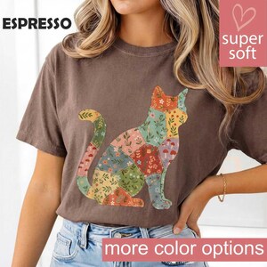 May include: A brown short-sleeve t-shirt featuring a graphic of a cat composed of various patchwork sections with floral and mushroom patterns. The text ESPRESSO is printed in the top left corner, and the text super soft is in the top right.