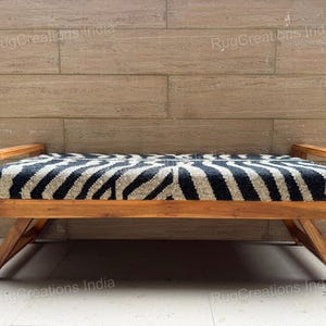 May include: A wooden bench featuring a rectangular seat upholstered in a black and white zebra-striped fabric. The bench has a natural wood frame with angled legs and flat armrests. The text RugCreations India is visible on the image.