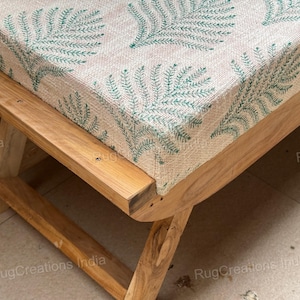 May include: A wooden bench featuring a rectangular cushion with a beige base and a repeating green fern leaf pattern. The bench has a natural wood grain finish and a sturdy frame with angled legs, providing a stable base for the upholstered seat.