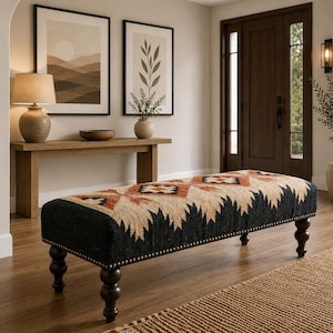 May include: A rectangular upholstered bench featuring a woven fabric top with a geometric pattern in shades of black, tan, and burnt orange. The bench is supported by four dark brown turned wooden legs and accented with a row of metallic nailhead trim.