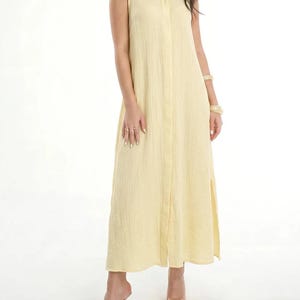Könnte beinhalten: Ein ärmelloses, bodenlanges, hellgelbes Hemdblusenkleid mit Kragen und einer strukturierten, knittrigen Stoffoberfläche. Das Kleid hat eine gerade Silhouette mit Seitenschlitzen am Saum und sorgt für ein schlichtes und klares Erscheinungsbild.