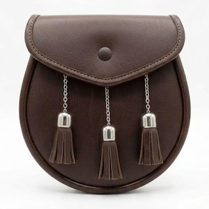 May include: A brown leather sporran with a flap closure and a button. The sporran has three decorative tassels hanging from silver chains. The bag is a rounded shape.