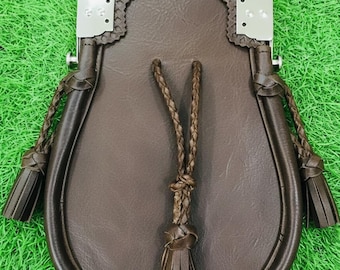 May include: A brown leather sporran with a silver metal top and decorative tassels. The sporran has a rounded bottom and a drawstring closure. The background is green.
