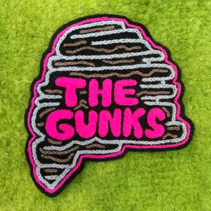 May include: A black and pink embroidered patch with the text "THE GUNKS" in pink lettering.