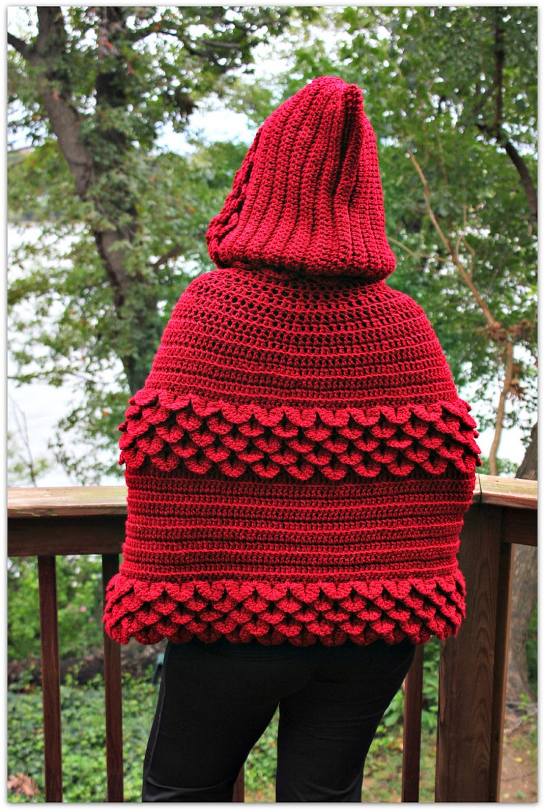 May include: A red crocheted hooded cape with a scalloped edge. The cape is made with a textured stitch and has a deep hood.