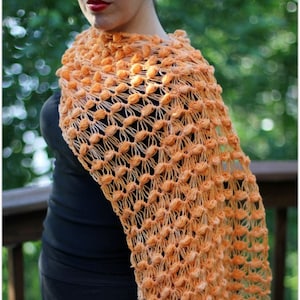 Könnte beinhalten: Ein gehäkeltes Tuch in einem pfirsichfarbenen Orange mit einem zarten Lochmuster. Das Tuch ist über die Schultern einer Person gelegt.