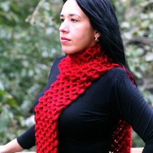 Puede incluir: Una mujer lleva una bufanda de ganchillo roja con una camisa negra de manga larga. La bufanda est&aacute; hecha con un punto texturizado que se asemeja a escamas.