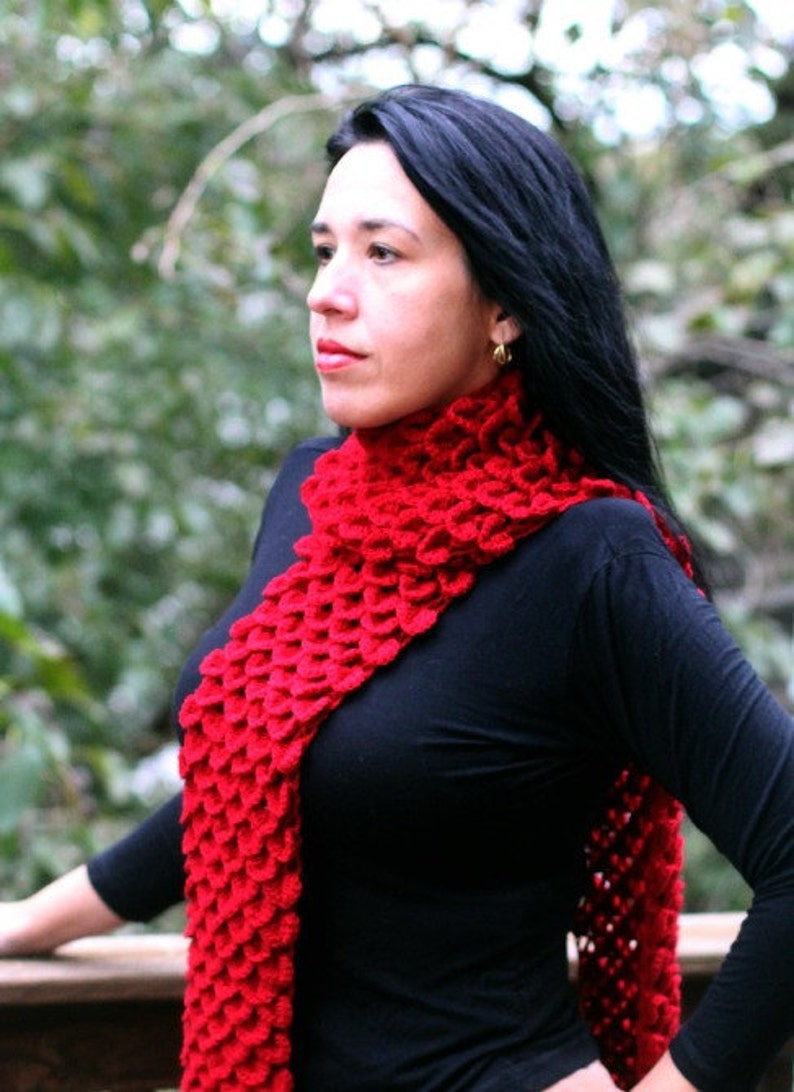 Puede incluir: Una mujer lleva una bufanda de ganchillo roja con una camisa negra de manga larga. La bufanda est&aacute; hecha con un punto texturizado que se asemeja a escamas.