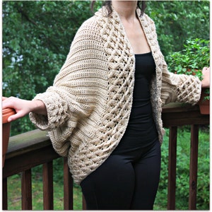 May include: A beige, open-front crochet cardigan with a textured pattern. The sleeves are wide and the cardigan has a relaxed fit. The garment is made of a soft, possibly wool or cotton yarn.