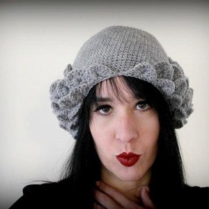 May include: A gray crocheted hat with a scalloped edge. The hat is worn by a person with long black hair and red lipstick.