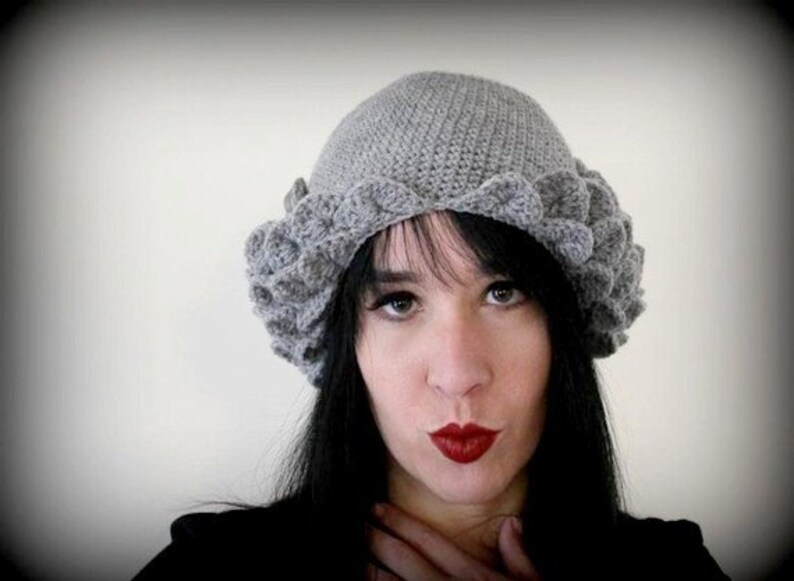 May include: A gray crocheted hat with a scalloped edge. The hat is worn by a person with long black hair and red lipstick.