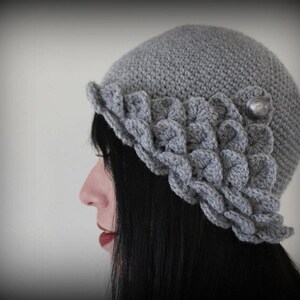 May include: A gray crocheted hat with a scalloped brim and a silver button accent.