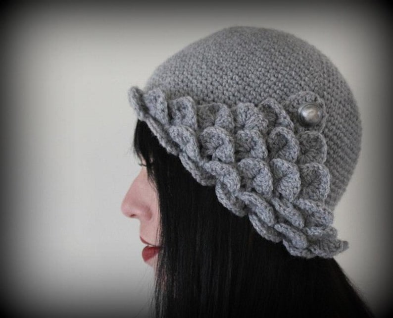 May include: A gray crocheted hat with a scalloped brim and a silver button accent.