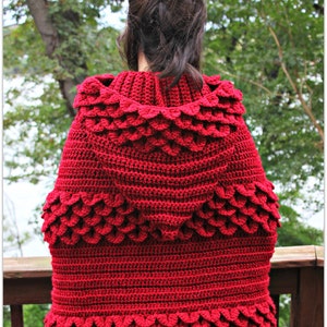 May include: A red crocheted hooded cape with a scale pattern. The cape is made with a textured stitch and has a wide, flowing hood.