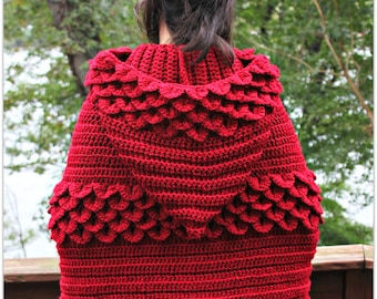 Könnte beinhalten: Eine rote gehäkelte Kapuzenjacke mit einem Schuppenmuster. Die Jacke wird von einer Person mit langen braunen Haaren getragen.