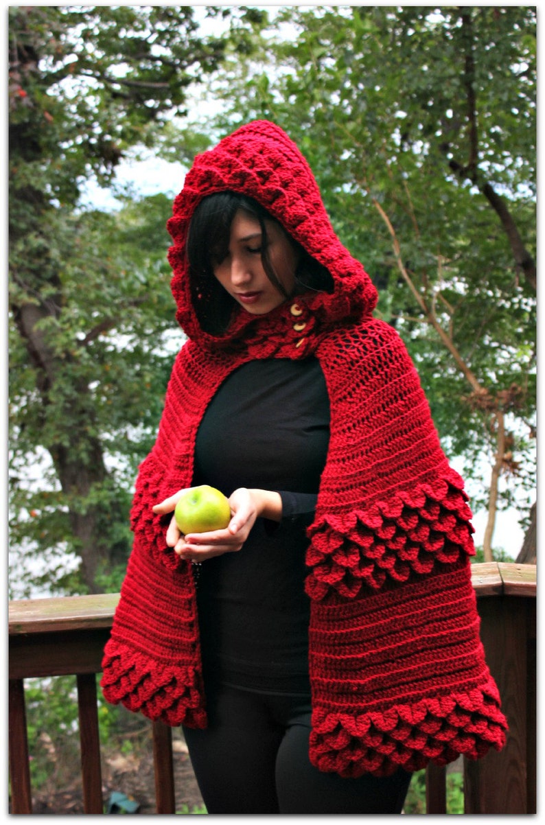 May include: A red crocheted hooded cape with a scalloped edge and a green apple held in the hand of the person wearing the cape.
