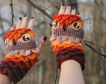 May include: A pair of crocheted owl fingerless gloves in a brown, orange and cream colour scheme. The gloves feature a crocheted owl face with large eyes and a beak.