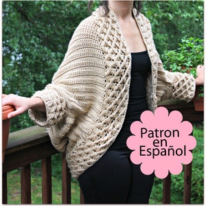 May include: A beige crochet cardigan with a cable stitch pattern. The cardigan has a wide, open neckline and long sleeves. The text "Patron en Español" is visible in the image.