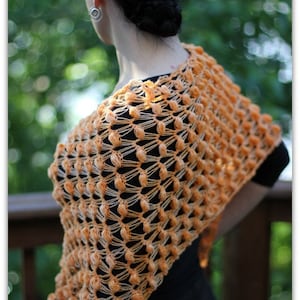 Könnte beinhalten: Ein orangefarbener gehäkelter Schal mit einem strukturierten, offenen Design. Der Schal ist über den Schultern drapiert und zeigt ein Muster aus erhabenen, abgerundeten Maschen. Die Farbe ist ein warmer, einladender Orangeton, perfekt, um jedem Outfit einen Hauch von handgefertigtem Charme zu verleihen.