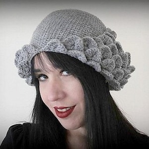 May include: A gray crocheted hat with a unique scalloped design. The hat is worn by a person with long black hair.
