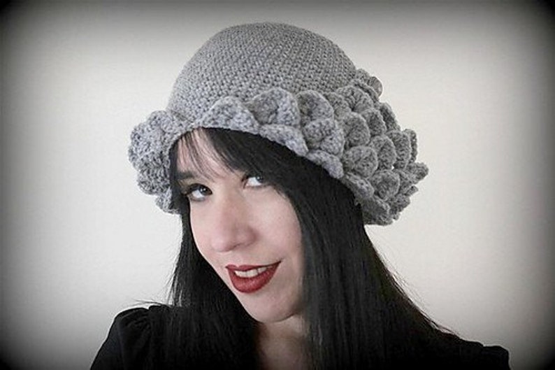 May include: A gray crocheted hat with a unique scalloped design. The hat is worn by a person with long black hair.