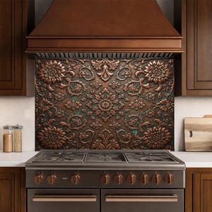 May include: A copper-colored backsplash with a floral pattern is installed above a stainless steel stove. The backsplash features a detailed, embossed design with large flowers and swirling vines. The kitchen also includes a copper range hood and dark brown cabinets.