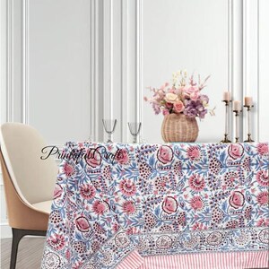 Peut inclure: Une nappe blanche avec un motif floral rose et bleu recouvre une table. La nappe a une bordure rayée. Un panier en osier avec des fleurs, deux verres à vin et des bougies sont sur la table. Le texte "Printofab Crafts" est sur la nappe.