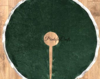 Puede incluir: Una falda redonda de árbol de Navidad verde oscuro con un ribete de flecos plateados. La falda tiene una abertura para el tronco del árbol y presenta el texto "Printafa Crafts" en un diseño circular.