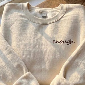 Sudadera minimalista con texto pequeño en el pecho, cuello redondo blanco.