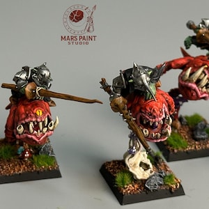 May include: Five miniature fantasy figures. Each figure features a red, toothy creature with a warrior riding on top. The warriors wear silver helmets and wield spears. The figures are mounted on square bases with green and brown terrain.