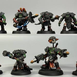 May include: A collection of miniature Ork figures, hand-painted with green skin, black armor, and various weapons. The figures are posed on black bases, with details like red and orange accents. The Mars Paint Studio logo is visible in the background.