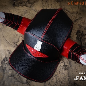 Puede incluir: Gorra de béisbol negra con detalles rojos y blancos, con un diseño único en forma de cuerno. La gorra tiene costuras rojas y un emblema blanco. Tallas disponibles: 53-56 cm, 57-60 cm y 61-63 cm. El texto "FAN CAP" es visible.