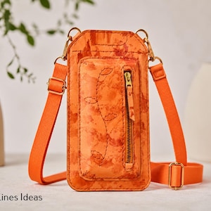 May include: A rectangular orange crossbody phone bag with a mottled texture and a stitched vine pattern. It features a vertical zipped front pocket with gold-tone hardware, an adjustable orange strap, and the text Crafted Lines Ideas.