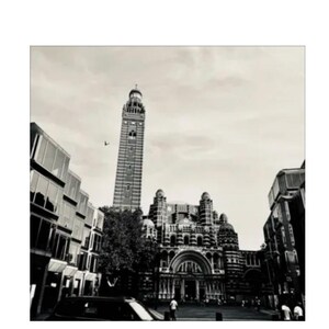Pode incluir: Fotografia a preto e branco de um edifício alto com uma torre do relógio, ladeado por outros edifícios. A imagem é tirada de um ângulo baixo, enfatizando a altura das estruturas, com um céu nublado.