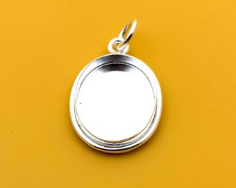 Peut inclure: Un pendentif ovale argenté avec une boucle en haut. Le pendentif présente une zone circulaire en retrait, probablement pour un motif. Le fond est d'un jaune chaud uni.